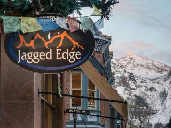 Sign for "Jagged Edge" with mountains in the background at dusk.