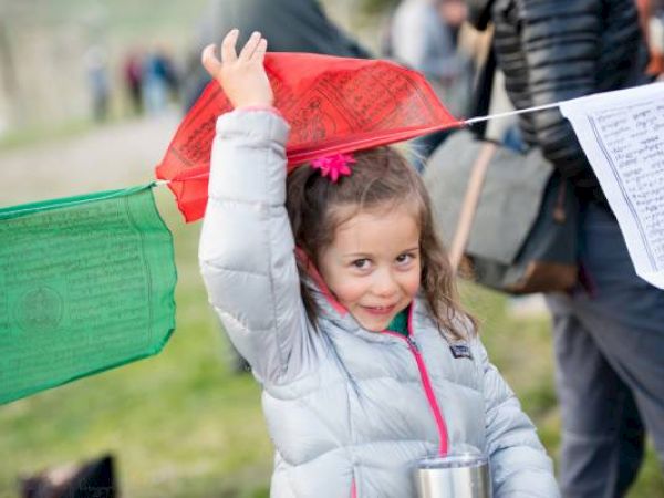 A smiling child holds a red flag, with people and sheets of music in the background.