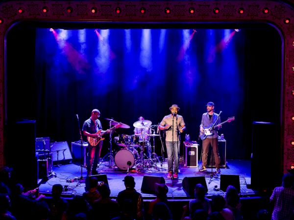 A live band performs on stage with colorful lighting, engaging an audience.
