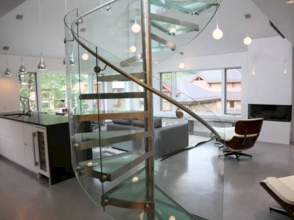 Modern interior with glass staircase, kitchen island, pendant lights, and furniture.