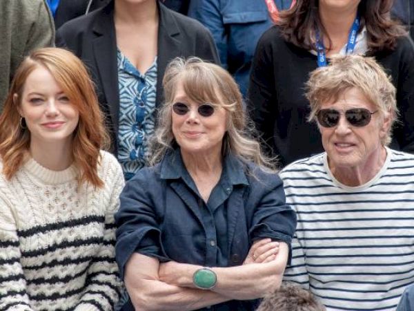 Three people smiling together, two women and a man, in casual clothes.