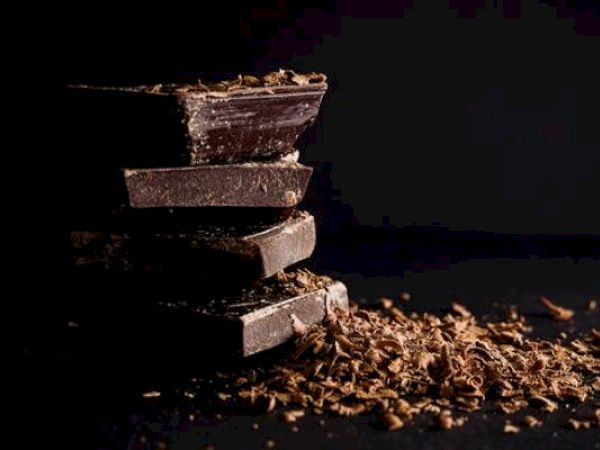 Stacked dark chocolate pieces with shavings on a dark surface.