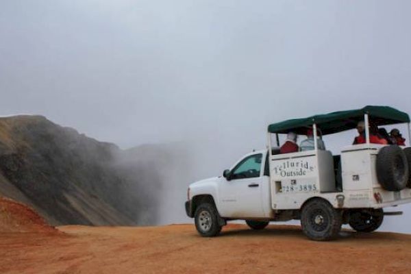 A modified truck carrying tourists on a dusty mountain road.