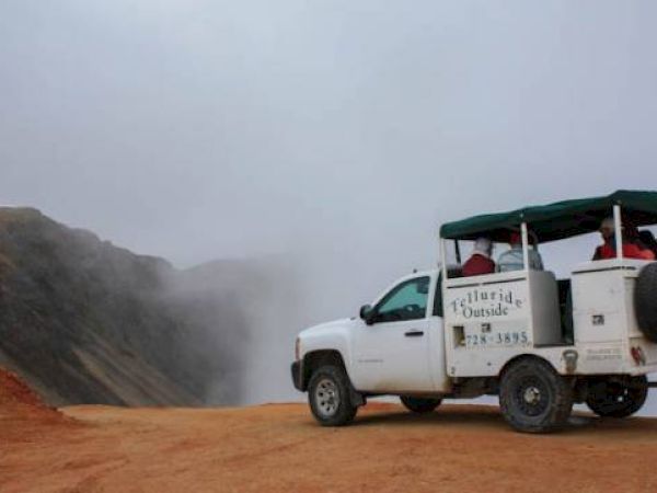 A modified truck carrying tourists on a dusty mountain road.