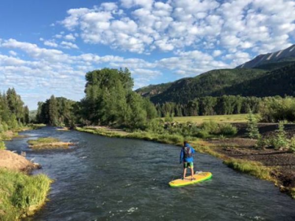 A person paddleboarding on a river with trees and mountains in the background.
