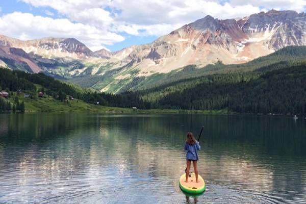 A person is paddleboarding on a tranquil lake with mountains in the background.