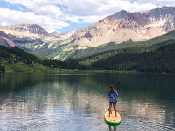 A person is paddleboarding on a tranquil lake with mountains in the background.