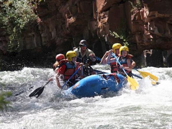 People are white-water rafting on a river, navigating through rapids.