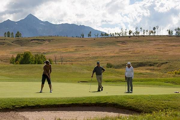 Golfers on a putting green with a mountainous backdrop.