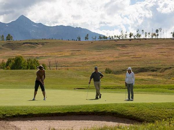 Golfers on a putting green with a mountainous backdrop.