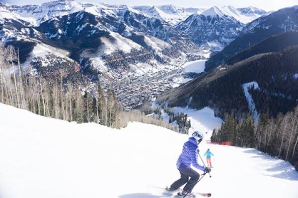 Person skiing down a snowy slope with mountains and a town in the background.