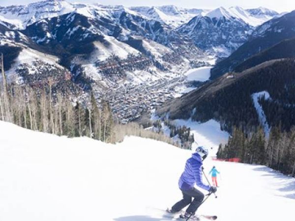 Person skiing down a snowy slope with mountains and a town in the background.