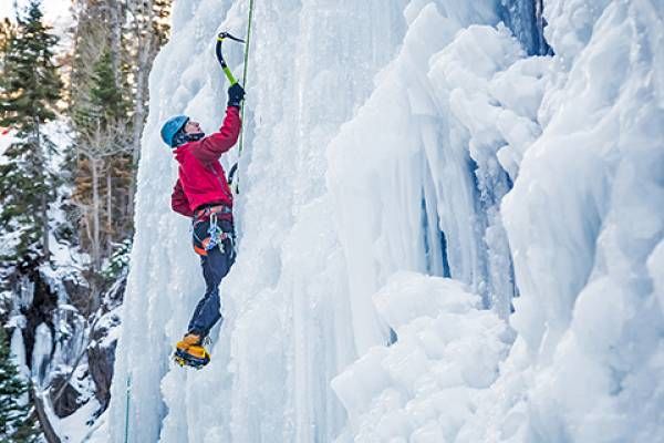 A person is ice climbing on a frozen waterfall using ice axes and crampons.