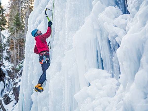 A person is ice climbing on a frozen waterfall using ice axes and crampons.