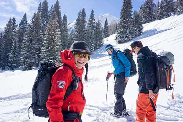 Three people in snow gear are hiking in a snowy mountain landscape.