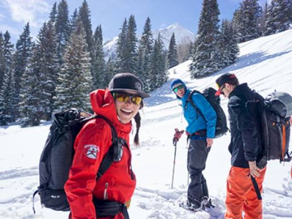 Three people in snow gear are hiking in a snowy mountain landscape.
