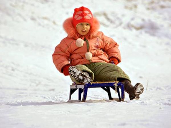 A child in warm winter clothes sits on a sled in the snow.
