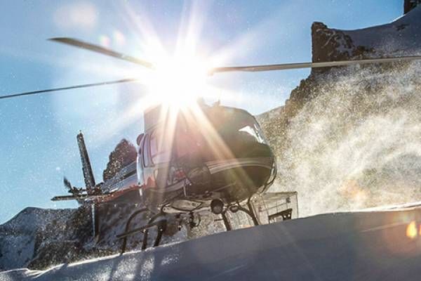 A helicopter lands on snowy terrain with the sun gleaming behind.