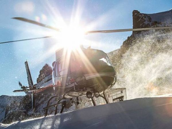A helicopter lands on snowy terrain with the sun gleaming behind.