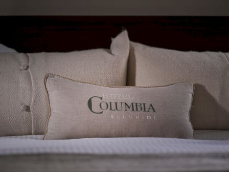 A set of beige pillows on a bed, with one pillow featuring the text 