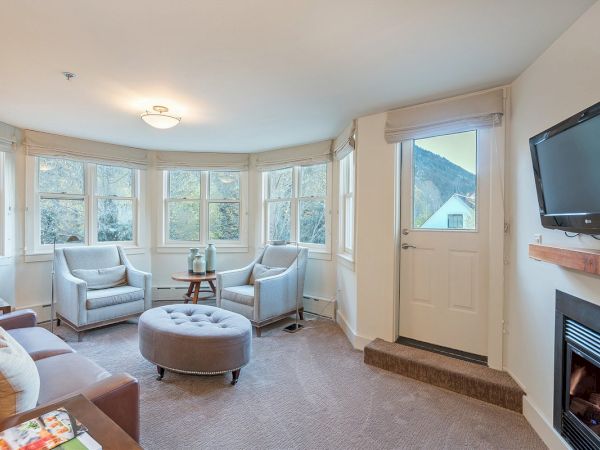A cozy Hotel Columbia Telluride living room with a fireplace, TV, chairs, ottoman, and a view of the mountains outside.