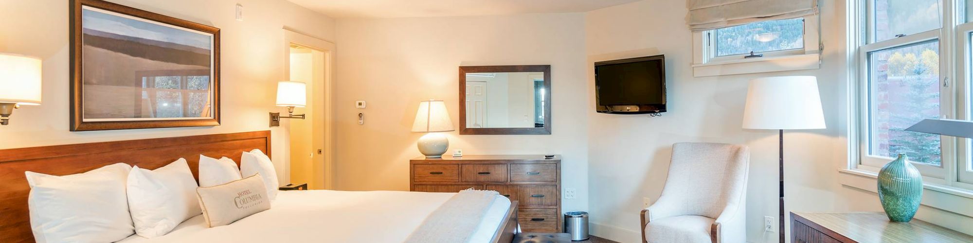 A neatly arranged Hotel Columbia Telluride room with a bed, chairs, lamps, and a window.