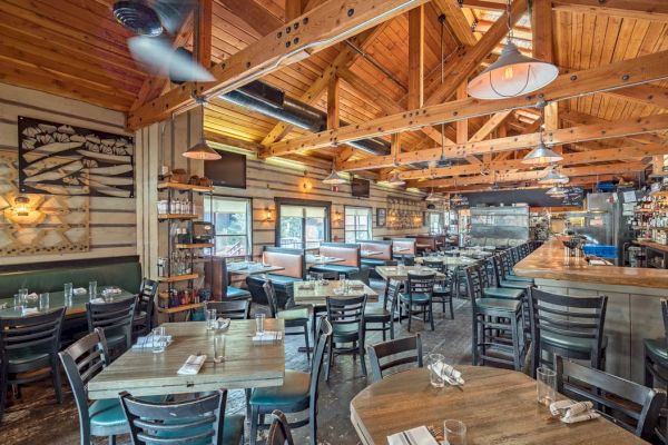 A cozy, wooden-interior restaurant with tables, chairs, a bar area, and ceiling fans.