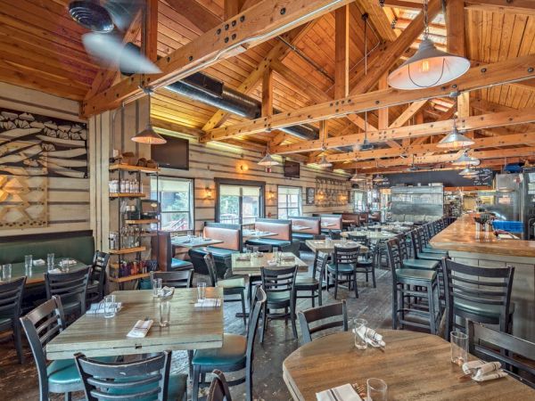 A cozy, wooden-interior restaurant with tables, chairs, a bar area, and ceiling fans.