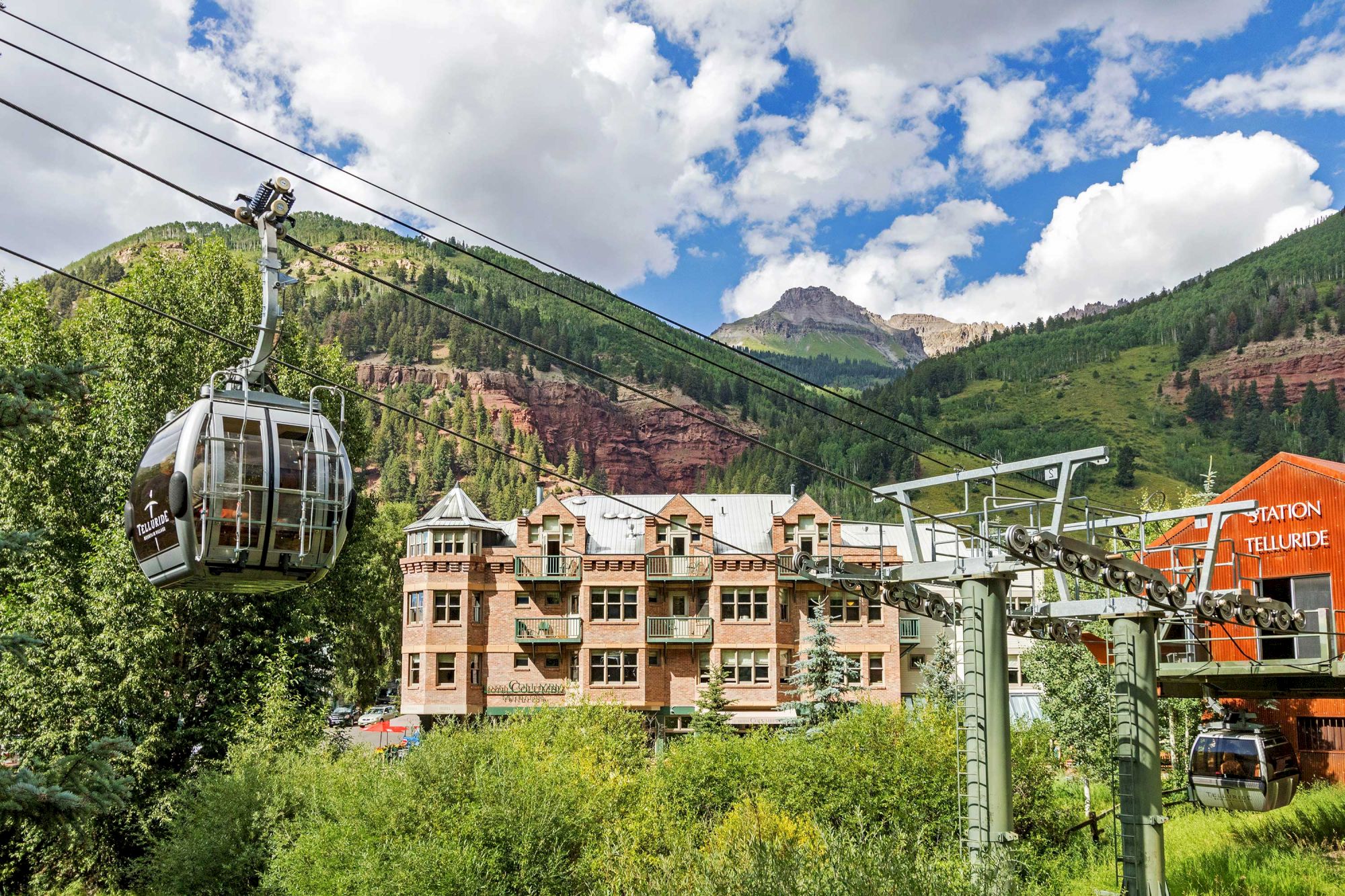 A gondola lift over Hotel Columbia Telluride with trees and a cloudy sky.