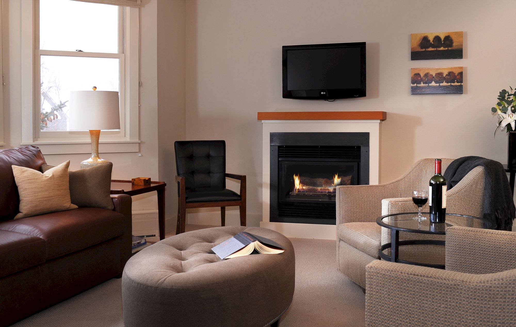 Cozy living room with a fireplace, sofa, chairs, TV, and a bottle of wine.