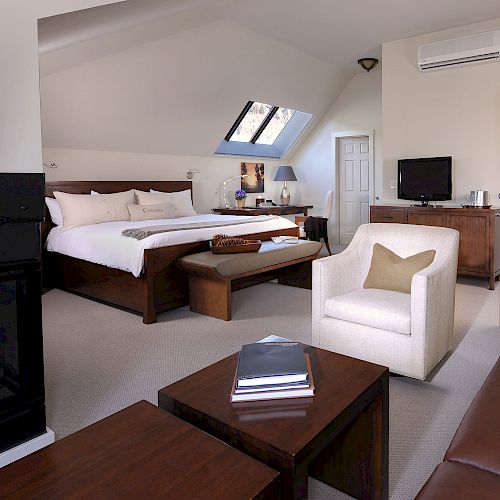 A cozy hotel room with a bed, fireplace, seating, and skylights.