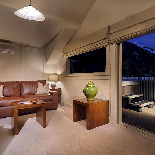 Cozy living room at dusk with sofa, table, lamps, and view of mountains through glass door.