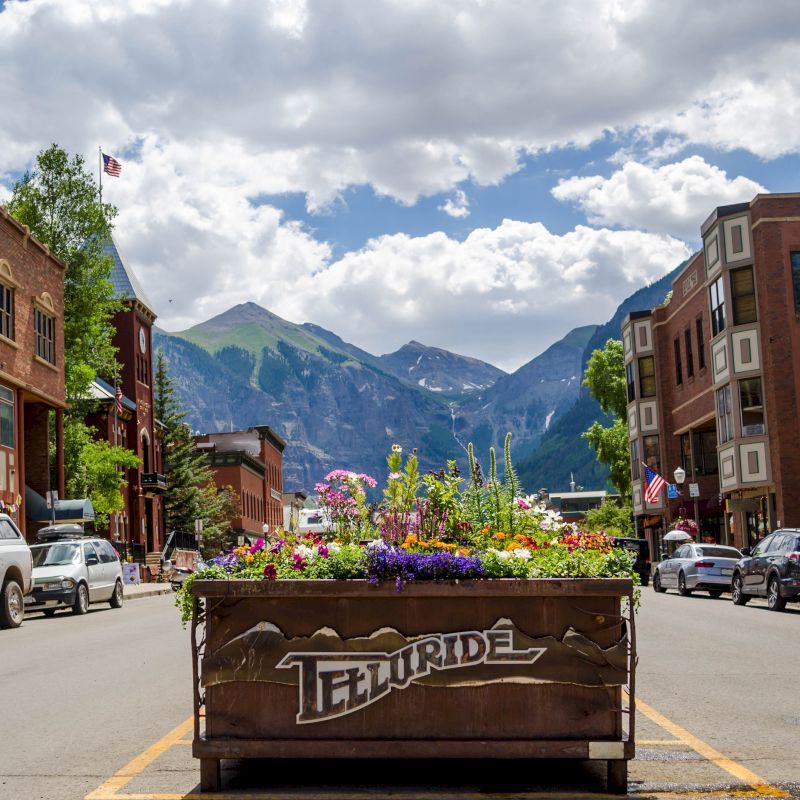 A picturesque street in Telluride with a floral planter, surrounded by historic buildings and mountains.