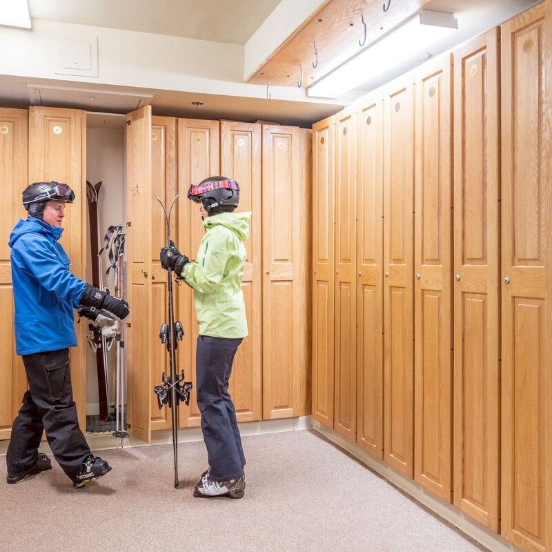 Two people in ski gear stand by wooden lockers, possibly prepping for skiing at the Hotel Columbia Telluride.